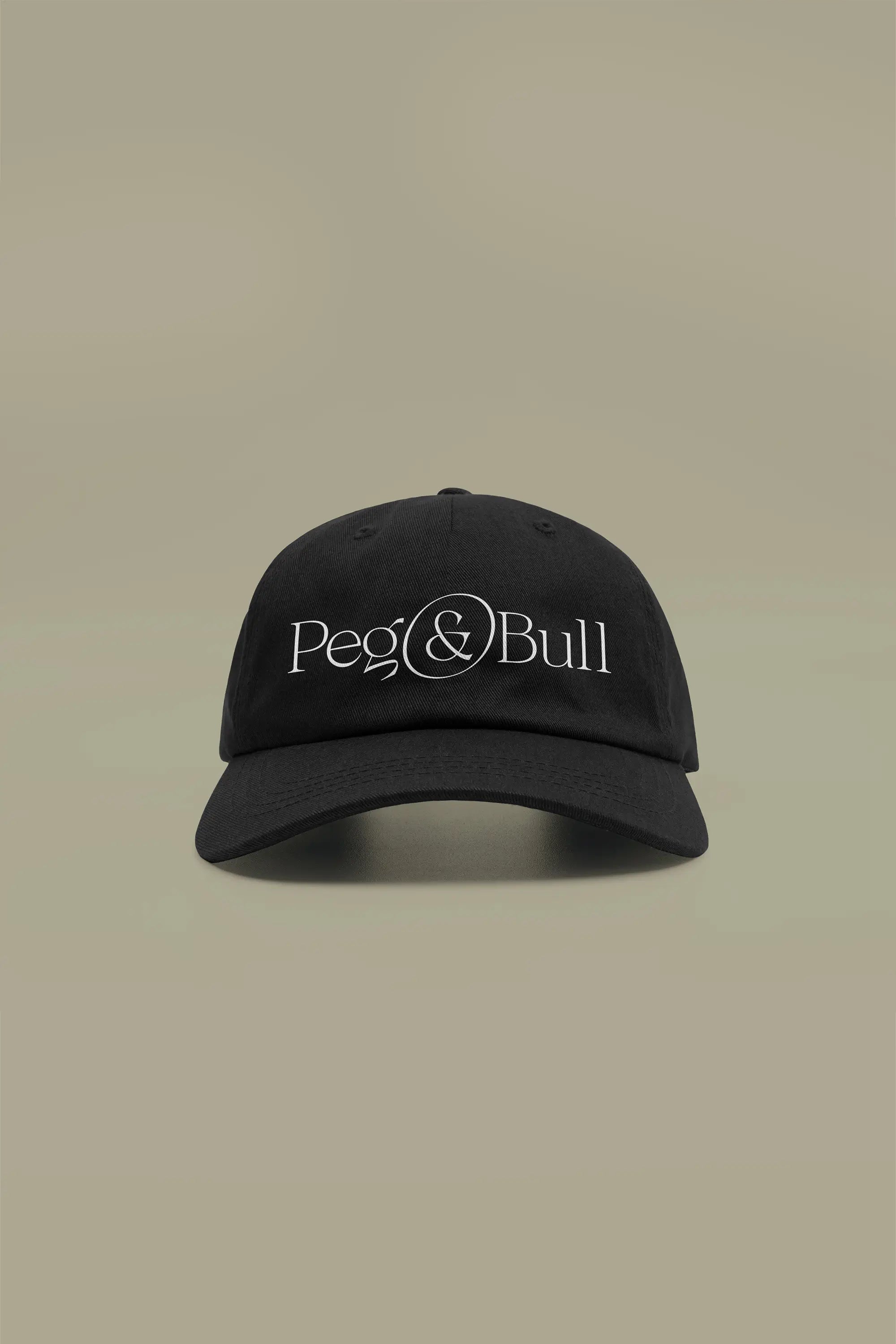 Black baseball cap with Peg & Bull logo on a beige background