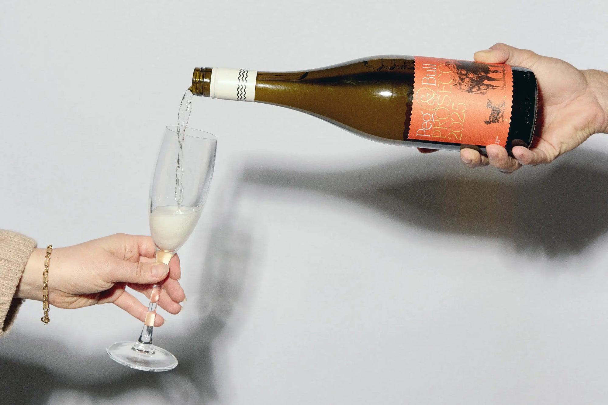 Person pouring Peg & Bull Prosecco from a bottle into a glass against a plain background